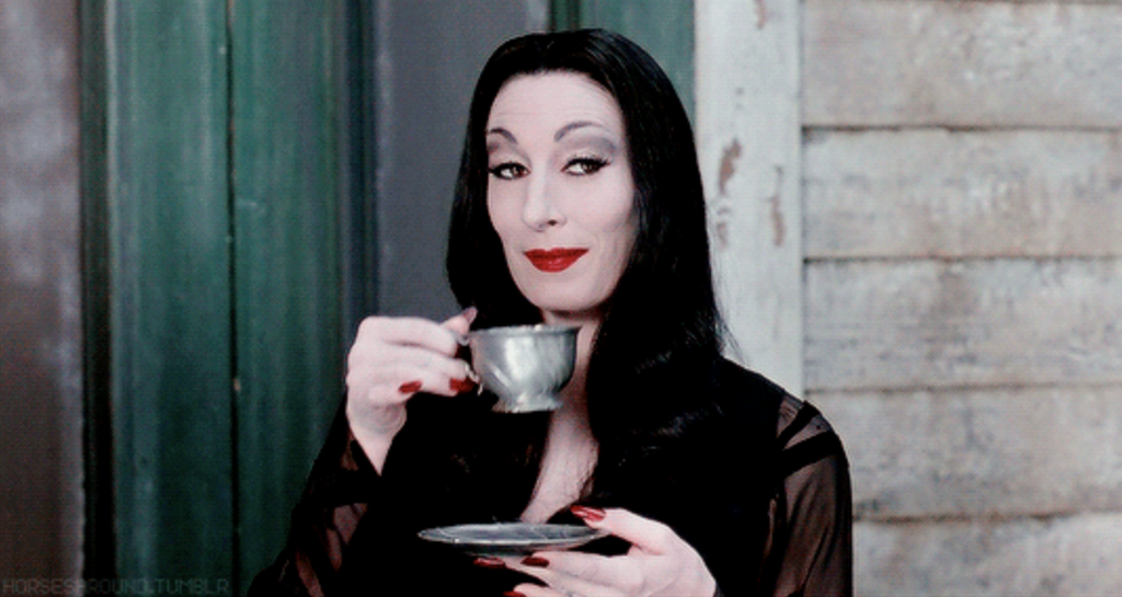 Morticia Addams smugly sips tea.